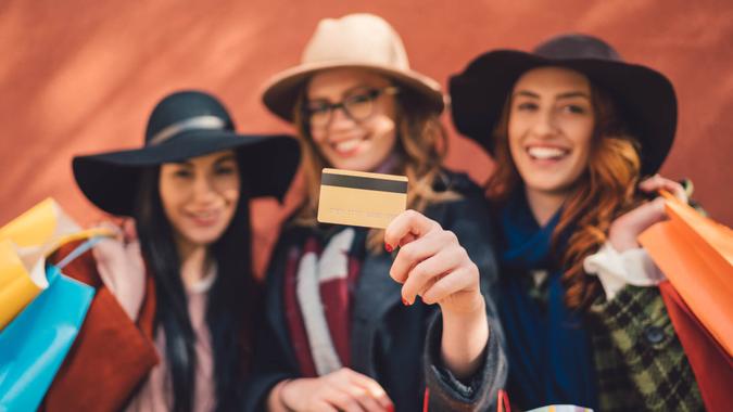 Young women holding paper bags and showing credit card to the camera.