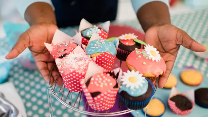 Close up hands hold out brightly decorated homemade cupcakes.