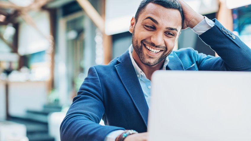 Young Middle Eastern ethnicity businessman looking at his laptop with happiness and excitement.