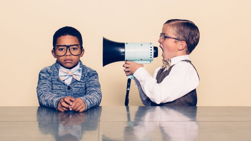 A young boy nerd shouts at the top of his voice to his co-worker through a megaphone trying to talk some sense into him but he is not listening and is ignoring him.