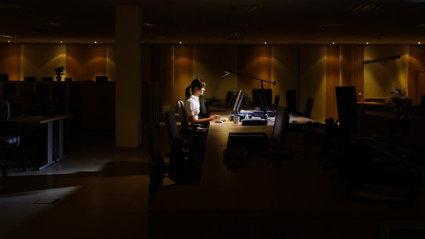 Side view of a young woman working on computer in dark office.
