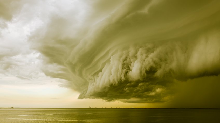 A mean looking huge storm cloud hovering over the ocean.