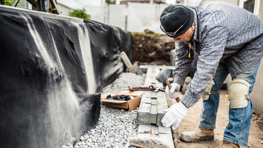 Senior man building a retaining wall with concrete blocks.