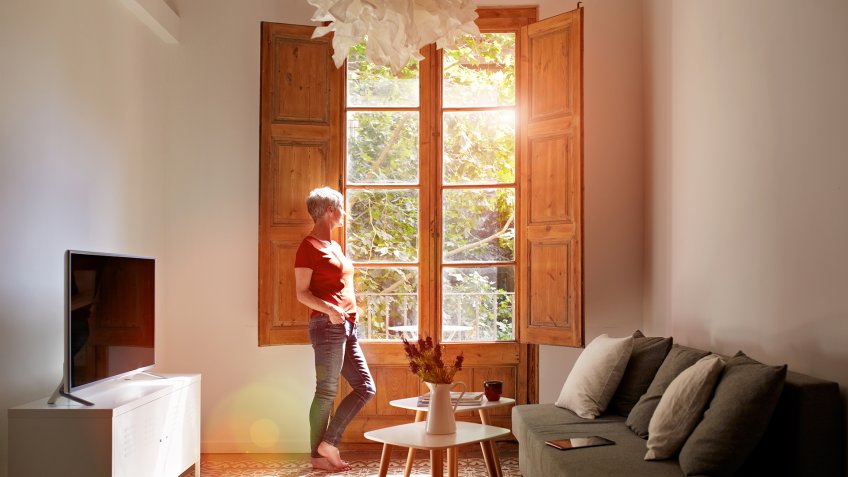 Shot of a mature woman standing by a window at home.