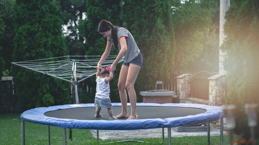 15 years old teenage girl and 17 months old baby playing on trampoline - jumping and having fun, enjoying each other.