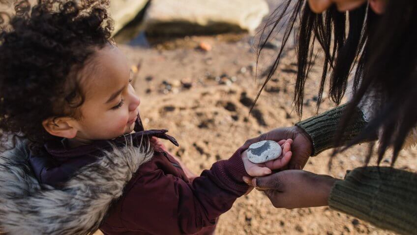 Close-up shot of a little girl handing a stone found on the beach to her mother.