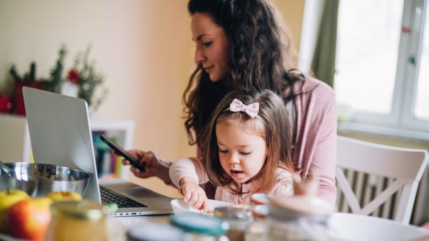 Mother work at home with little girl еating.