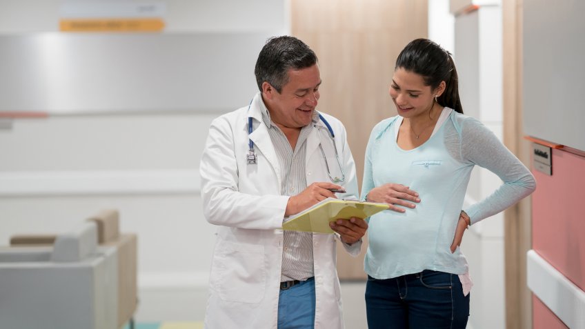 Pretty mother to be talking to friendly obstetician about her test results at the corridor of the hallway both looking very happy and smiling.