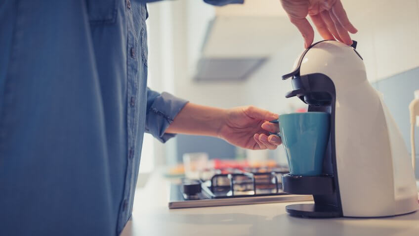 Young woman is making her morning coffee in her kitchen.