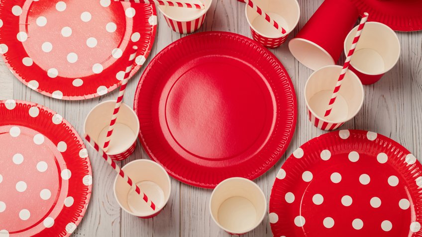 Disposable paper utensils of red and white color on a gray wooden background.