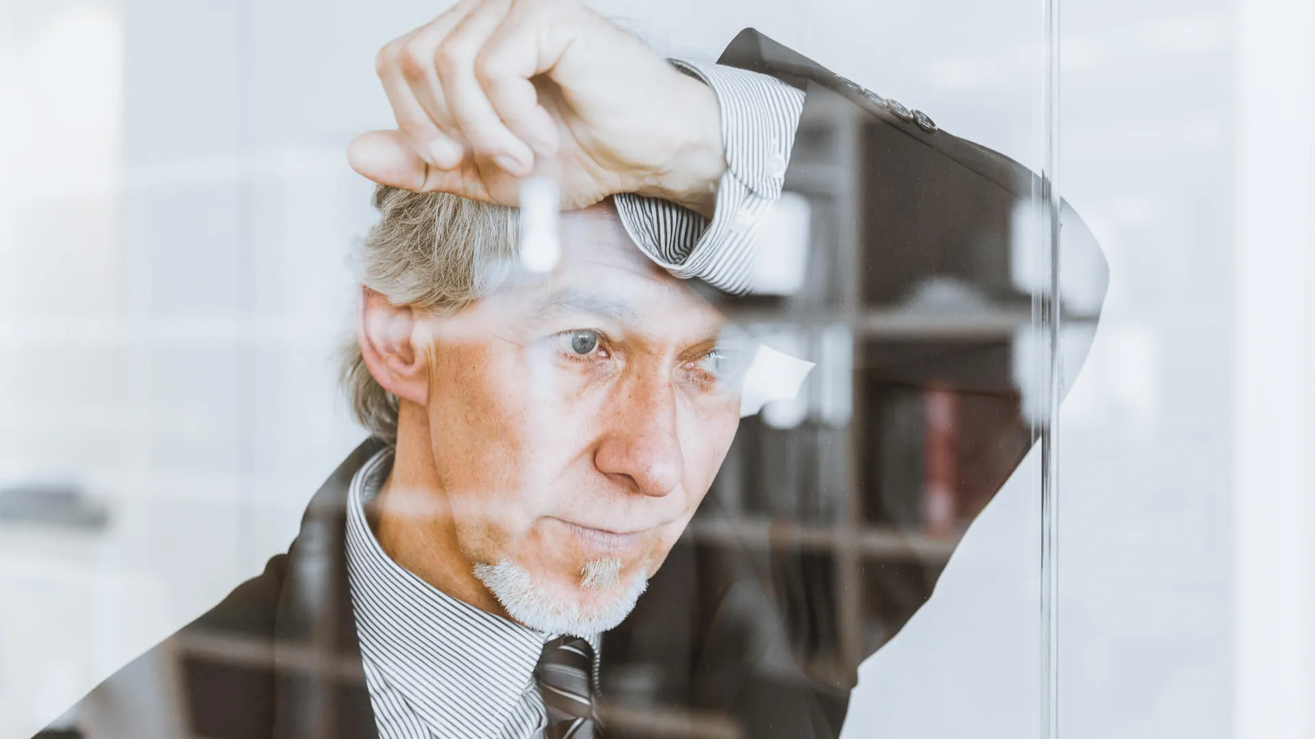 Pensive Senior Businessman, Manager leaning at the huge glass front window of modern conference room thinking with a serious, worried facial expression.