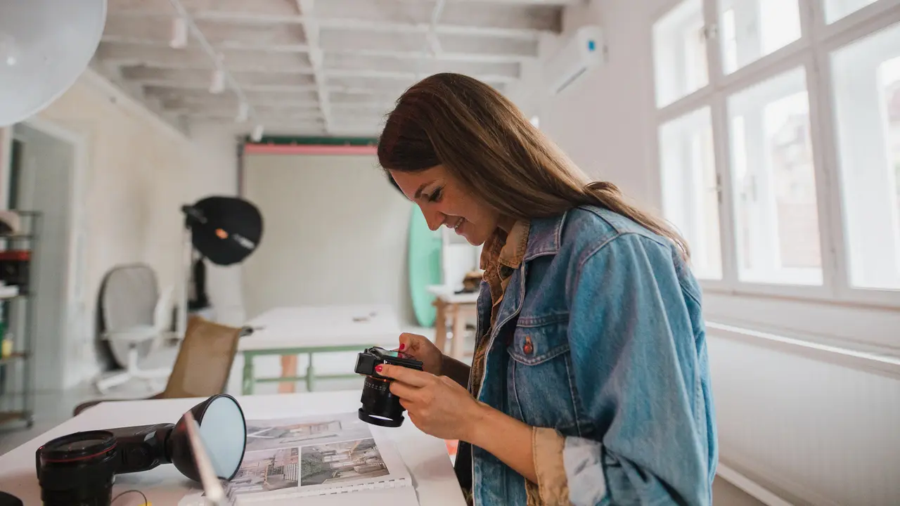 Photographer adjusting camera settings while standing in a studio surrounded by lighting equipment and photography gear