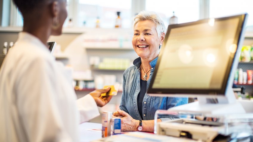 Female pharmacist returning the credit card to female client after receiving the payment.