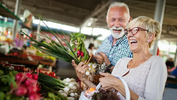 Smiling senior couple holding basket with vegetables at the grocery shop.