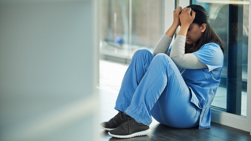 Shot of a young doctor sitting on the floor and looking distraught.