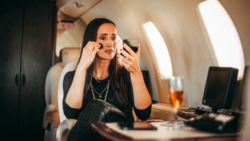 Rich and successful female putting her mascara on while traveling on a private airplane.