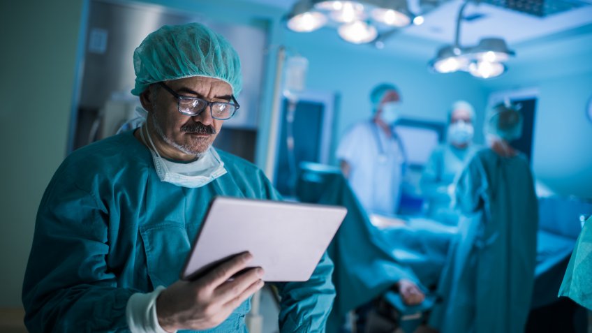 Mature doctor reading something from an e-reader in operating room.