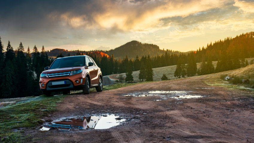 orange suv parked on the country road near forest in mountains at sunrise.