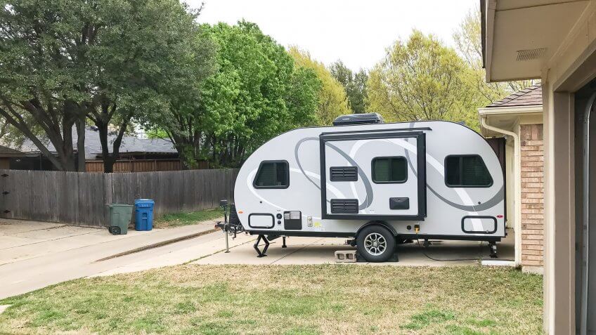 Side view of RV trailer parked at house garage backyard.