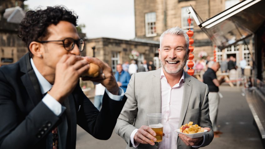 Two men tucking into their food from a food truck outside.