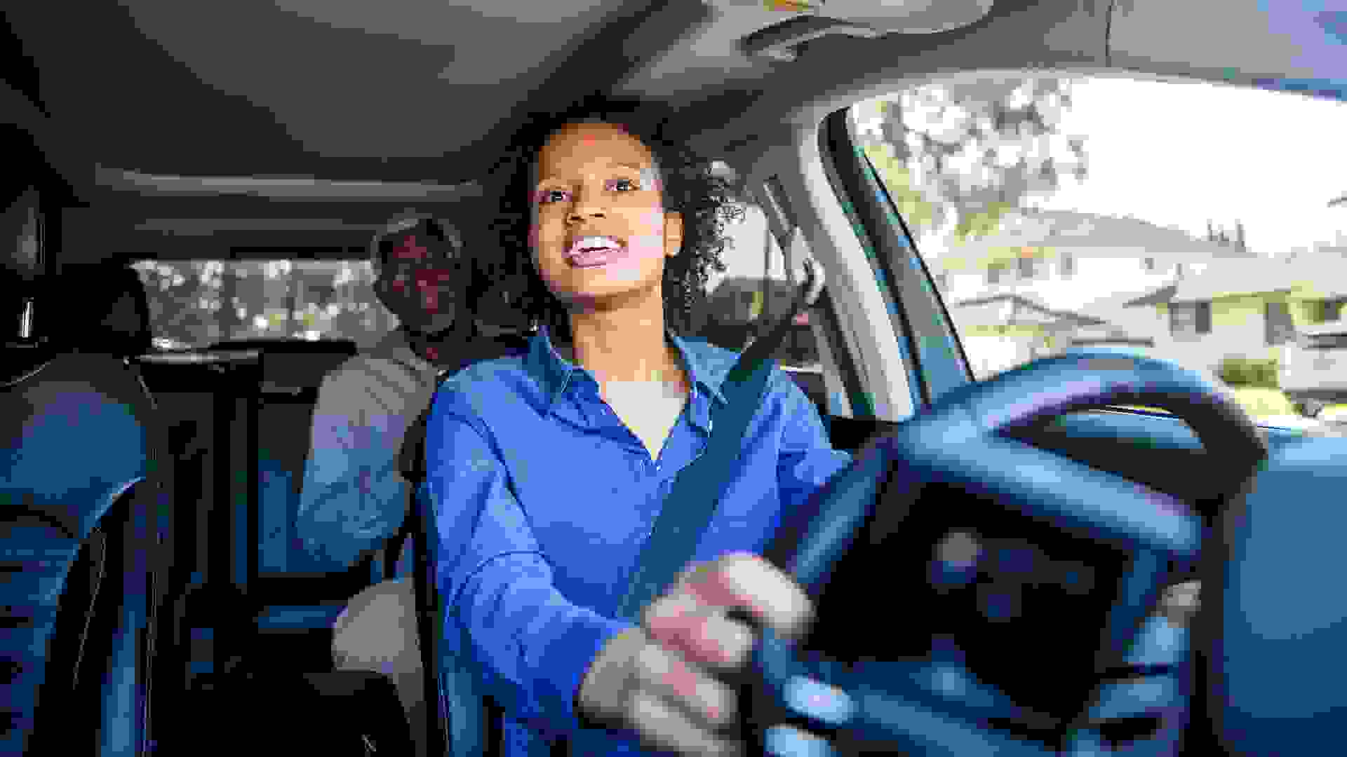 A young black woman drives a passenger in her car as a professional driver.