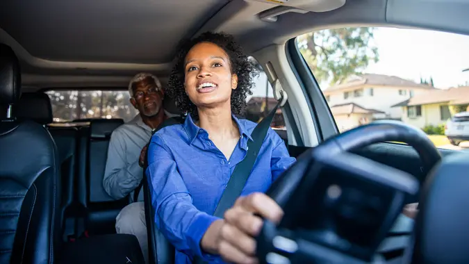 Une jeune femme noire conduit un passager dans sa voiture en tant que chauffeur professionnel.