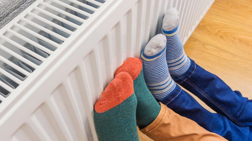 Woman and child wearing colorful pair of woolly socks warming cold feet in front of heating radiator in winter time.