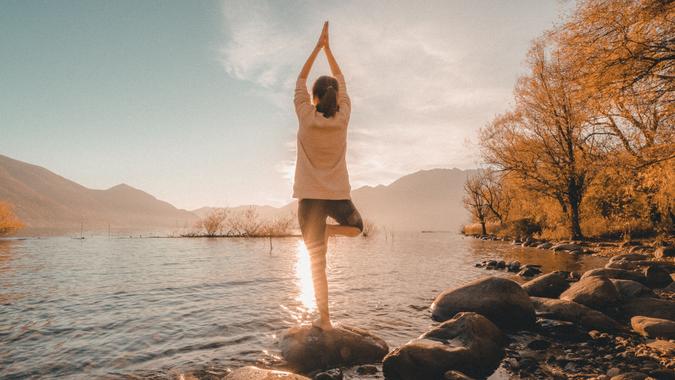 Young cheerful woman by the lake exercising yoga at sunset.