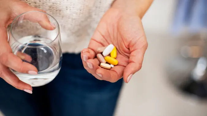 unrecognizable woman holding vitamins in one hand and water in the other.