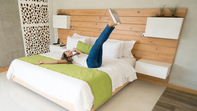 Excited traveling woman in her room at the hotel jumping on the bed and looking at the camera smiling.