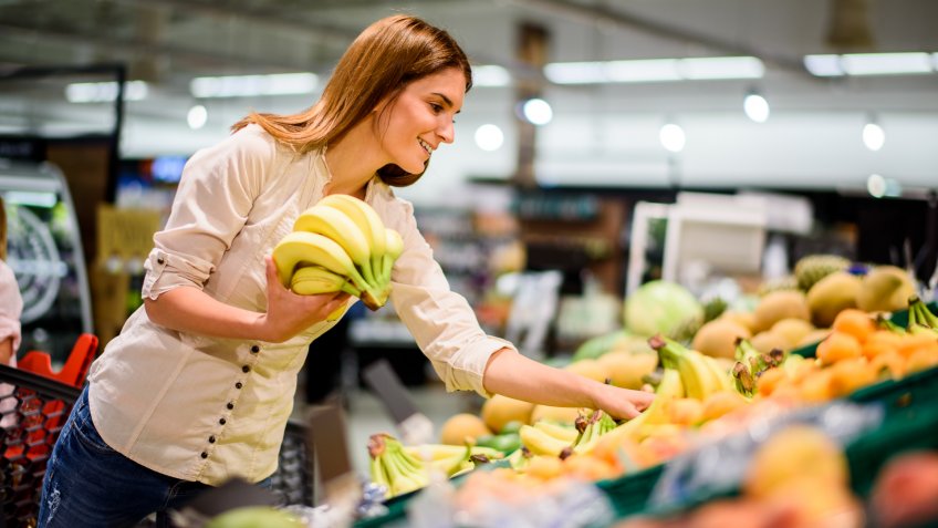 Young woman in the supermarket picking up bananas.