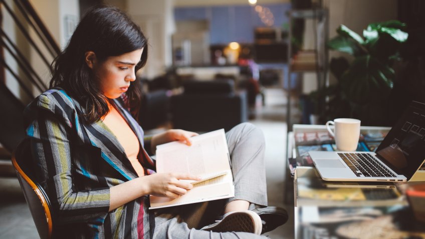 Young Latinx woman sitting at the desk in her Los Angeles apartment, doing her studies, going through books until late.