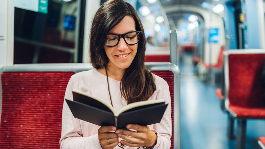 Young woman is reading a book in subway train.