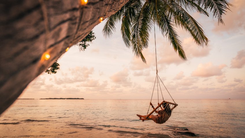 Young adult woman relaxing on a swing in a tropical paradise.