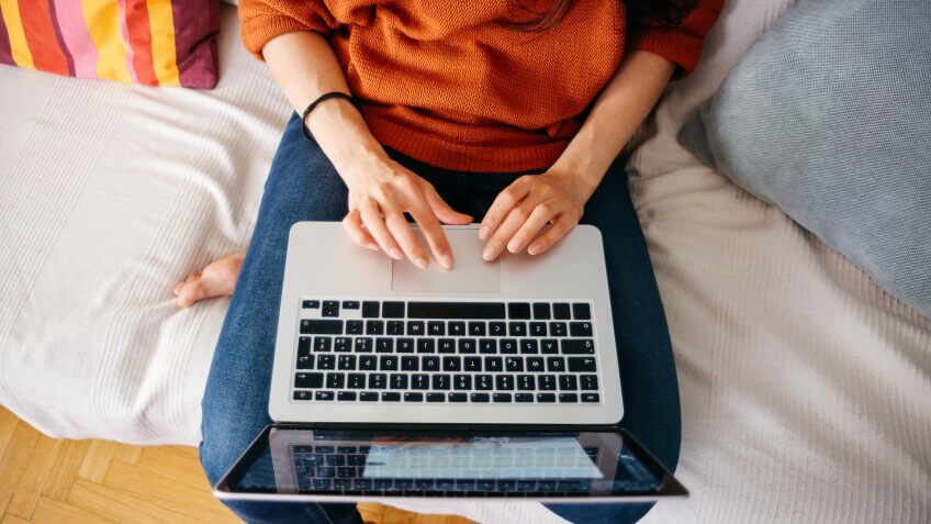 Closeup overhead image of a young woman sitting on the sofa at her home, using her laptop.