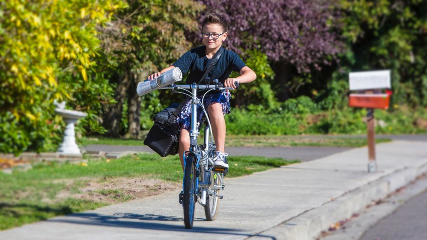 A young boy delivering newspapers on his bicycle - Image.