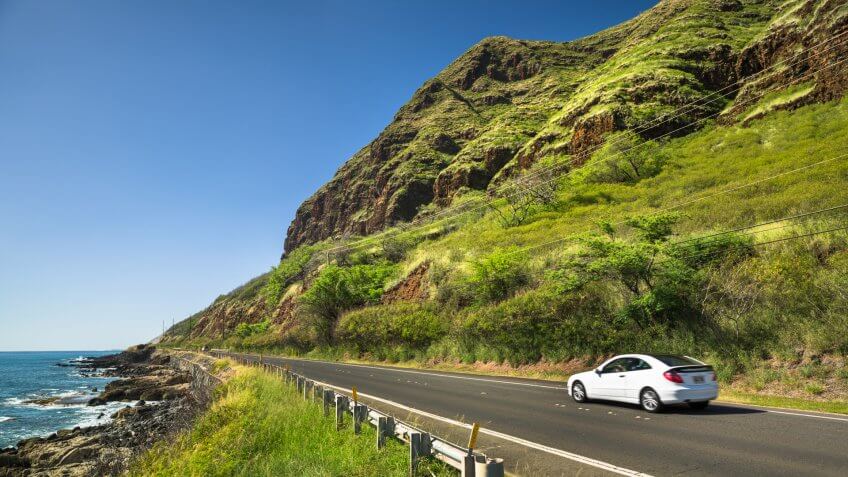 Haleiwa: Cars drive down the Farrington highway by Kaena Point State Park and Keawaula beach in Oahu Hawaii USA.