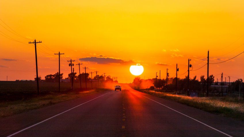Pickup truck heading home at sunset on West Texas country road.