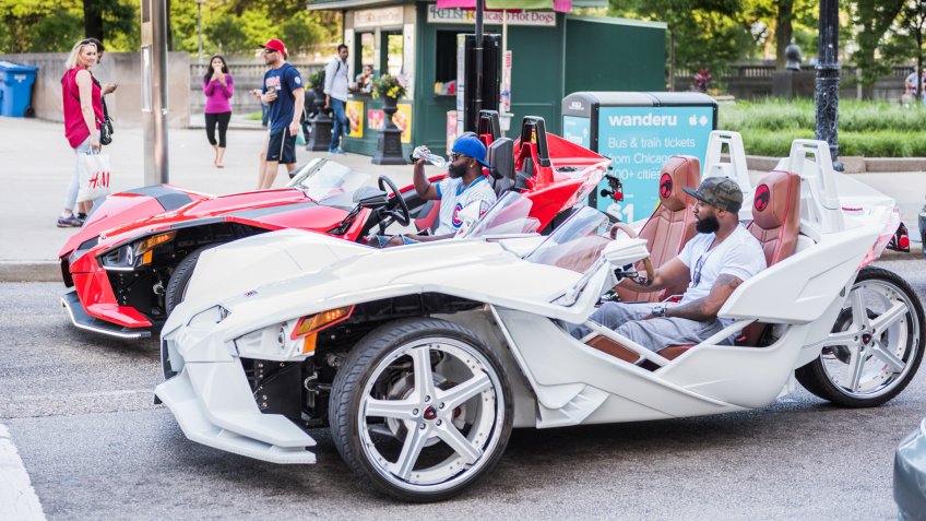 Chicago, USA - May 30, 2016: Two men with cubs shirt in flashy red and white Polaris Slingshot Ferrari sports cars on downtown street.