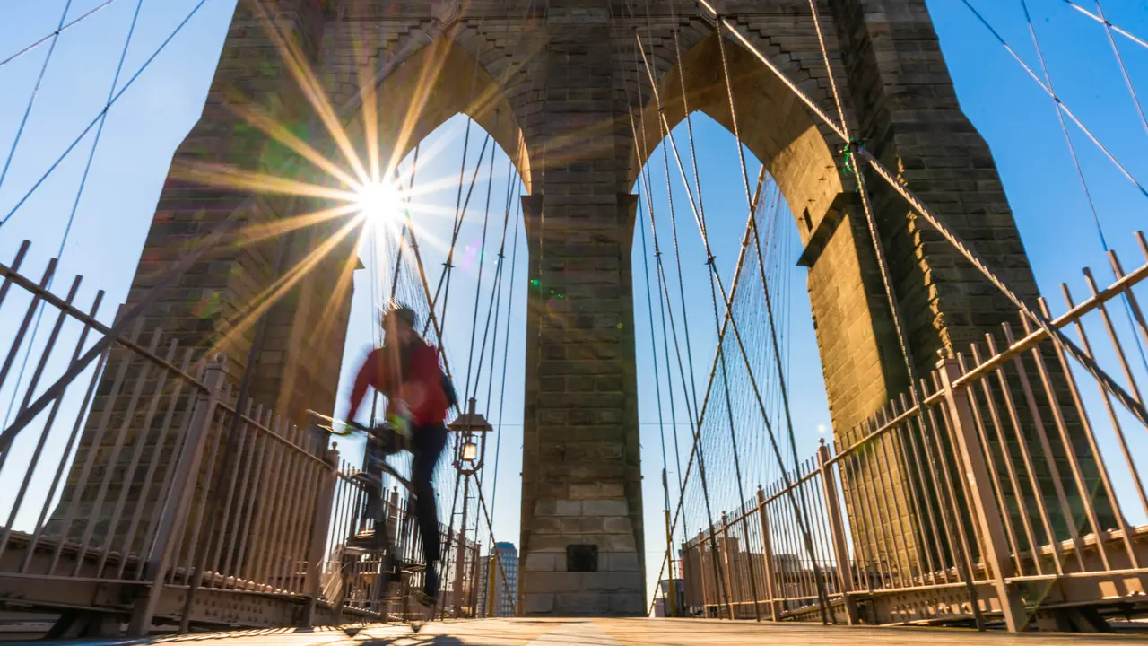 Scene of stop motion bicycle with Brooklyn bridge when sunrise, USA downtown skyline, Architecture and building with tourist concept.