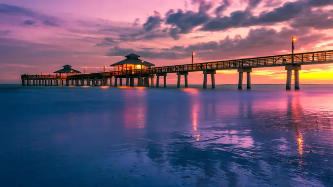 A colorful golden and purple sunset falls beneath the horizon at the Fort Myers Beach Pier in Florida, USA.