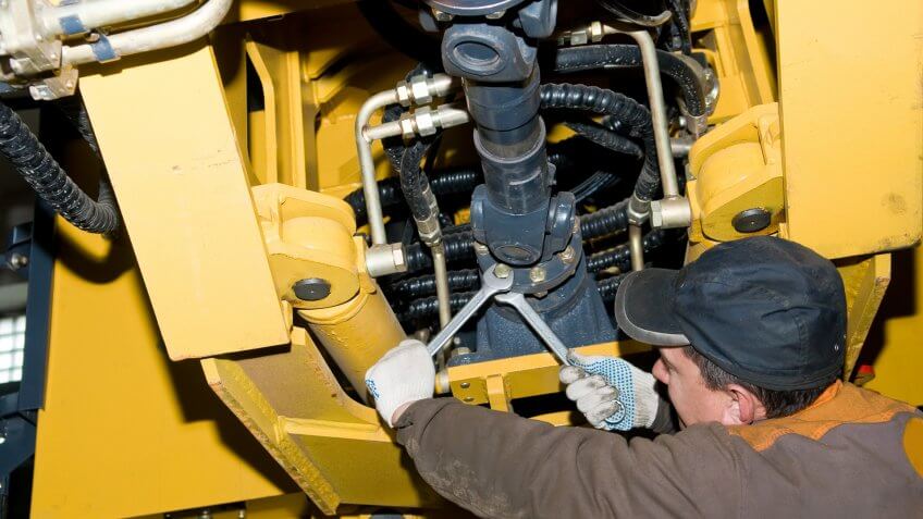 repairman worker screwing nuts of axle assembly in heavy wheel loader.