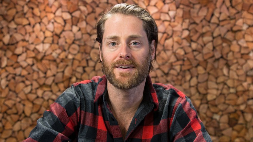 Hootsuite CEO Ryan Holmes stands in front of a wooden mural wall in the Hootsuite office, located in the Mount Pleasant neighbourhood of Vancouver.
