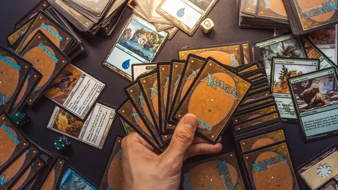 Bratislava/Slovakia - 06/13/2018: Magic the Gathering card playing game background with hand holding cards and cards and dice spread out behind - Image.