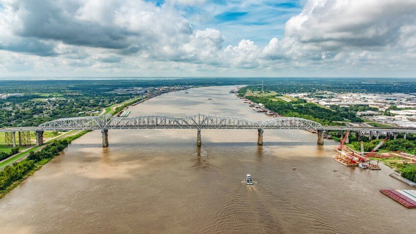 A bridge supporting both vehicles and a railway crossing the Mississippi River which is flanked on both sides by various industry located just north of New Orleans, Louisiana, shot from an altitude of about 600 feet over the river.