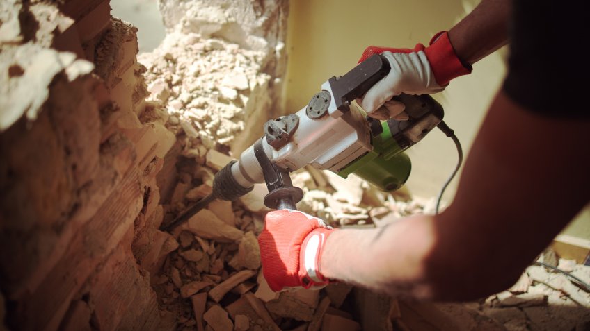 Home Renovation, Builder with hammer breaking wall indoors.