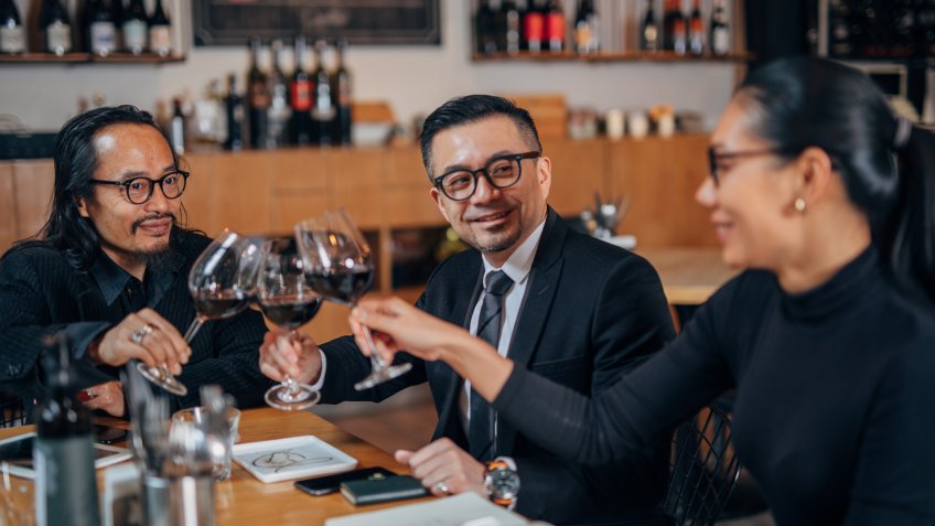 Three people, two men and woman, sitting in restaurant on business meeting, having a celebration toast.