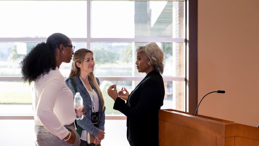 Mature female business conference keynote speaker talks with interested businesswomen after conference.