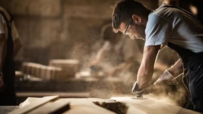 Manual worker using sander while working on a wood in carpentry workshop.