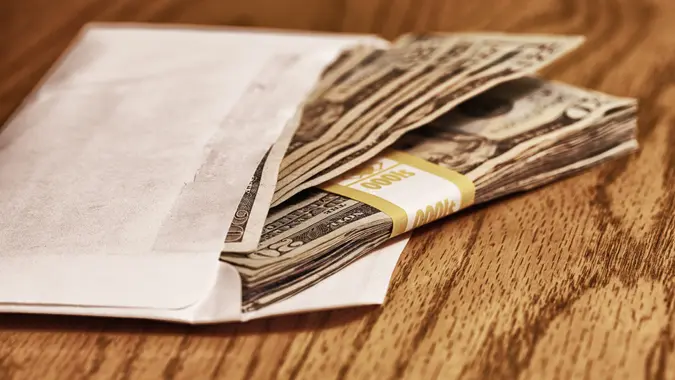 Stack of well-used United States twenty dollar bills stuffed into a grubby white envelope.
